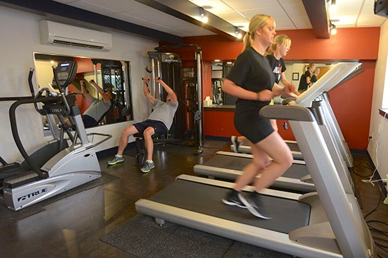 Keller workout room with workout equipment and mirrors, man lifting weights, two women running on treadmills